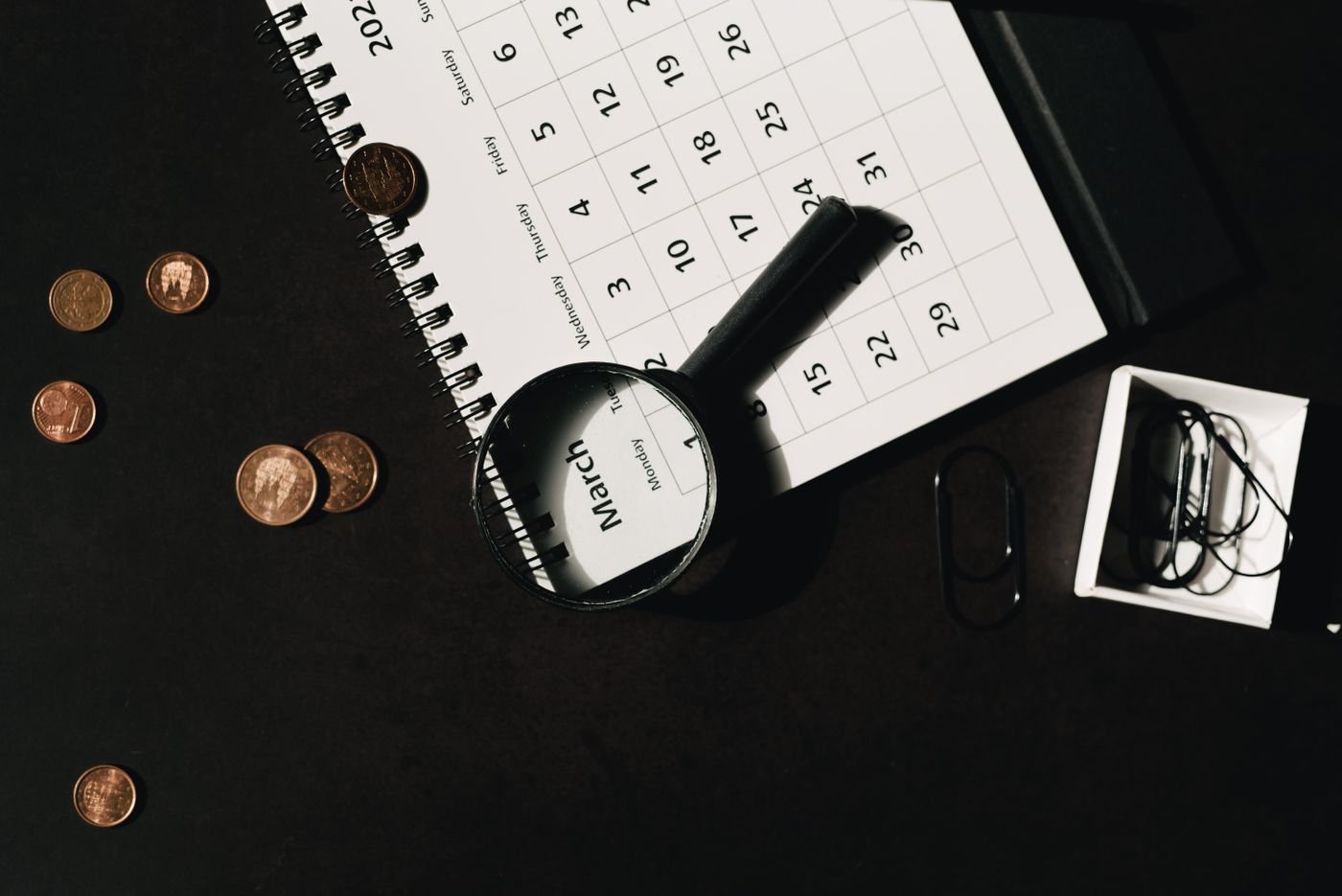 Coins beside a monthly calendar and magnifying glass