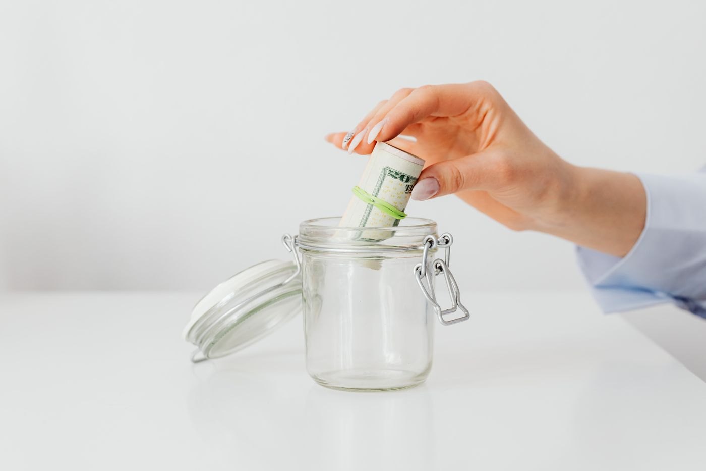 A hand putting banknotes into a glass savings jar