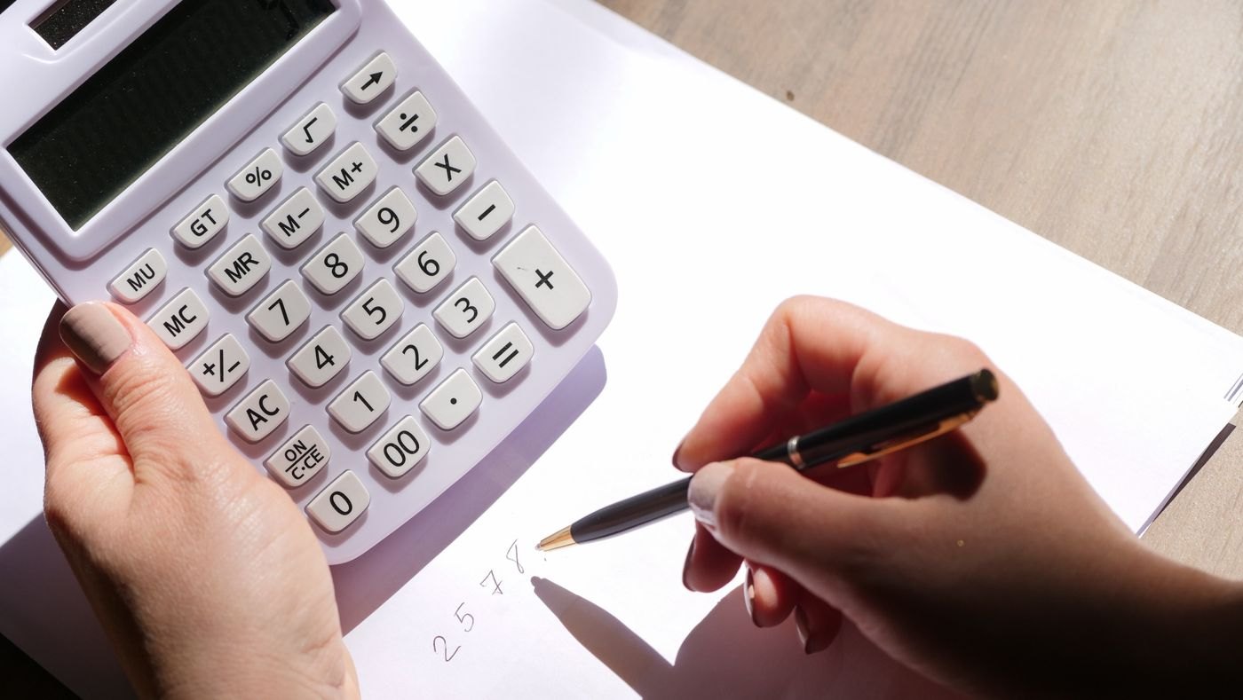 A hand holding a pen beside a calculator