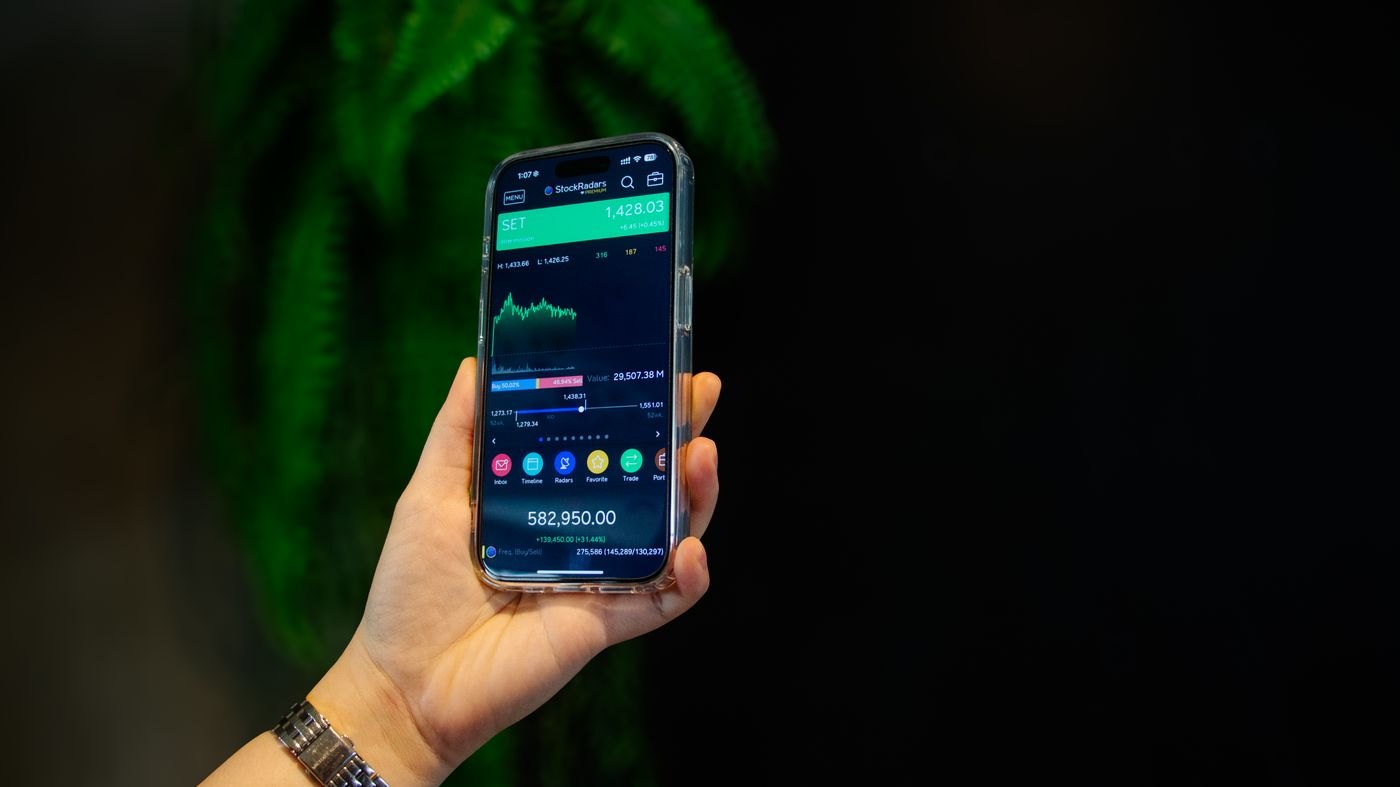 A hand holding a smartphone with a stock-market account display