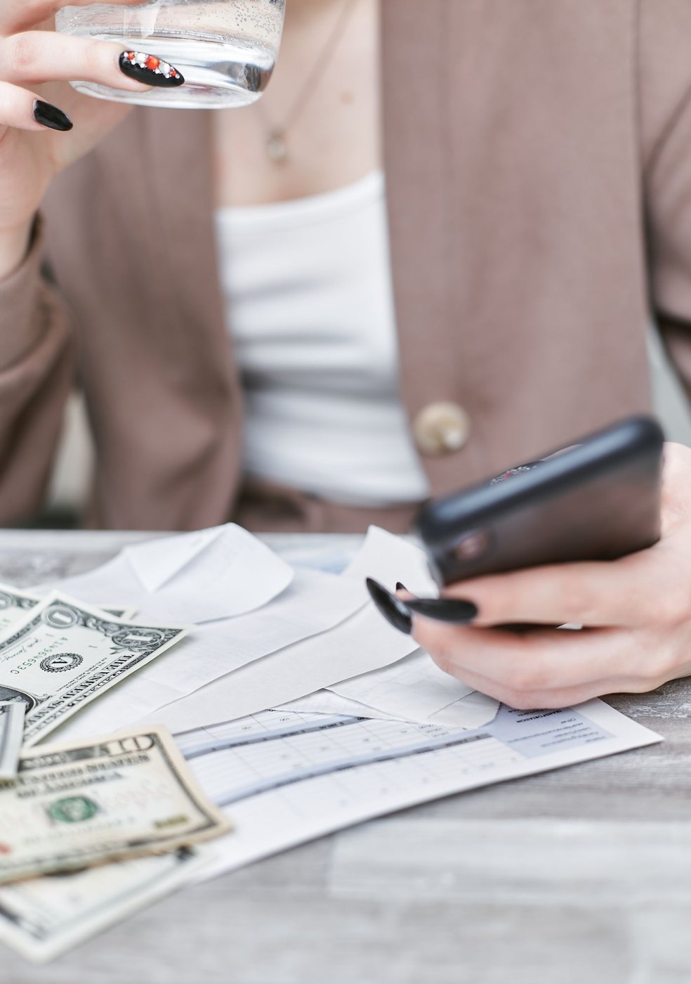 A person reviewing a phone beside financial paperwork